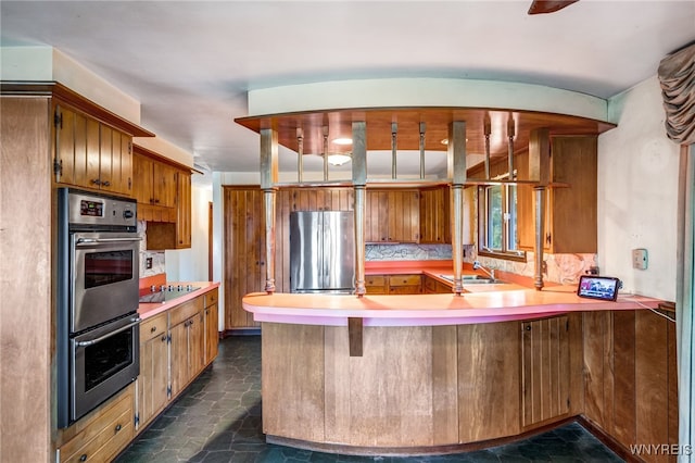 kitchen featuring kitchen peninsula, decorative backsplash, a kitchen bar, stainless steel appliances, and sink