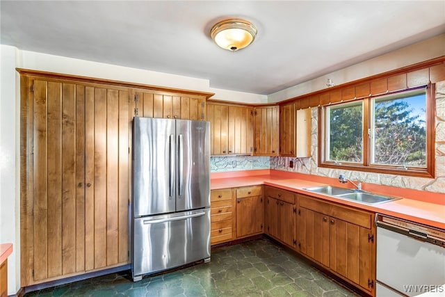 kitchen with white dishwasher, decorative backsplash, sink, and stainless steel refrigerator