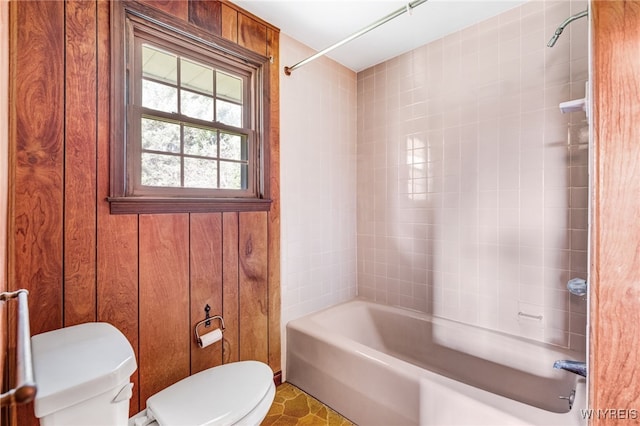 bathroom featuring toilet, tiled shower / bath, and wooden walls