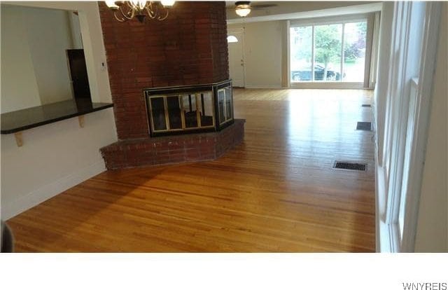 unfurnished living room with ceiling fan with notable chandelier, hardwood / wood-style flooring, and a brick fireplace