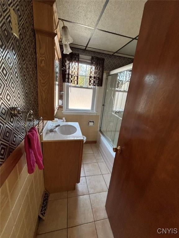 full bathroom with a drop ceiling, vanity, combined bath / shower with glass door, tile patterned flooring, and toilet