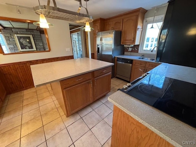 kitchen with a center island, sink, wooden walls, stainless steel dishwasher, and decorative light fixtures