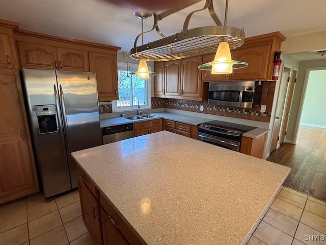 kitchen featuring hanging light fixtures, sink, light hardwood / wood-style flooring, decorative backsplash, and appliances with stainless steel finishes