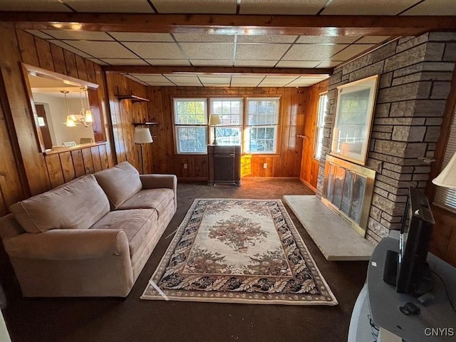 living room featuring a fireplace, wooden walls, a drop ceiling, and an inviting chandelier