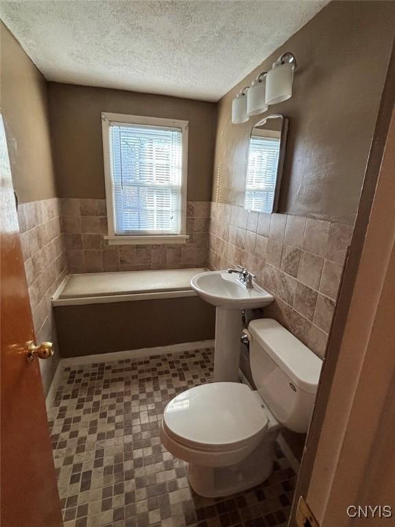 bathroom featuring a textured ceiling, tile walls, and toilet