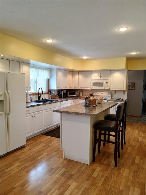 kitchen featuring sink, a center island, light hardwood / wood-style flooring, white appliances, and white cabinets