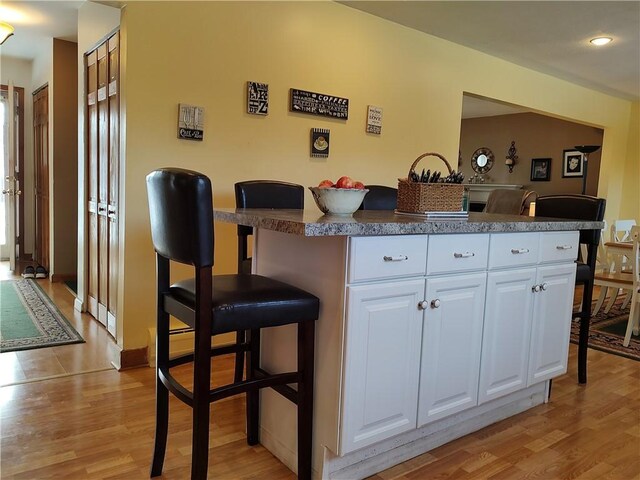 kitchen featuring a kitchen bar, white cabinets, and light wood-type flooring