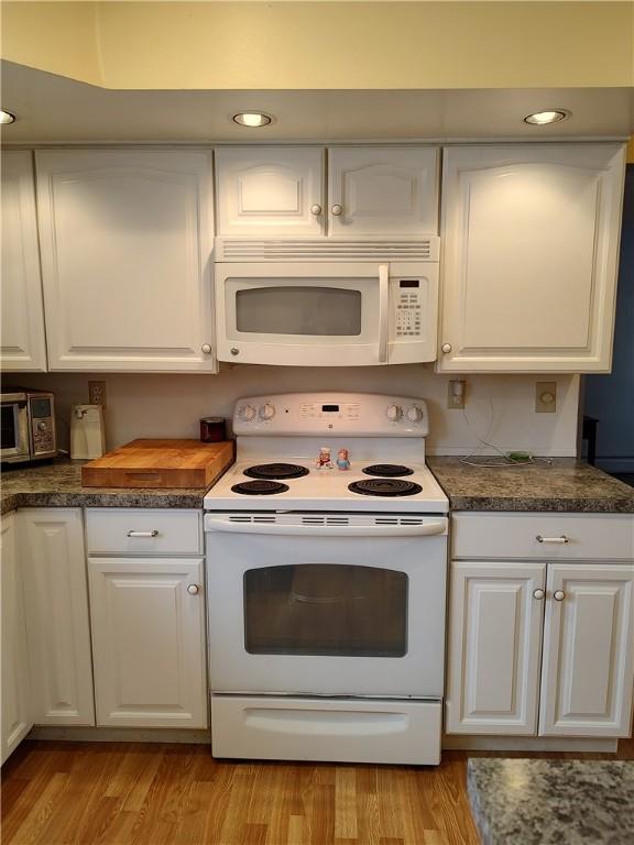 kitchen featuring white cabinets, light wood-type flooring, and white appliances