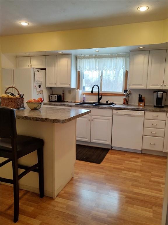 kitchen featuring white appliances, a kitchen breakfast bar, sink, light hardwood / wood-style floors, and white cabinetry