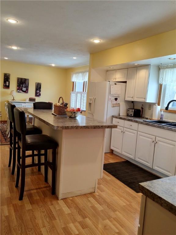 kitchen with a center island, sink, light hardwood / wood-style floors, a breakfast bar, and white cabinets