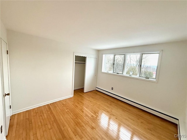 unfurnished bedroom featuring baseboard heating, a closet, and light hardwood / wood-style floors