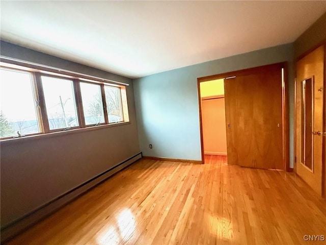 unfurnished bedroom with a closet, a baseboard heating unit, and light wood-type flooring