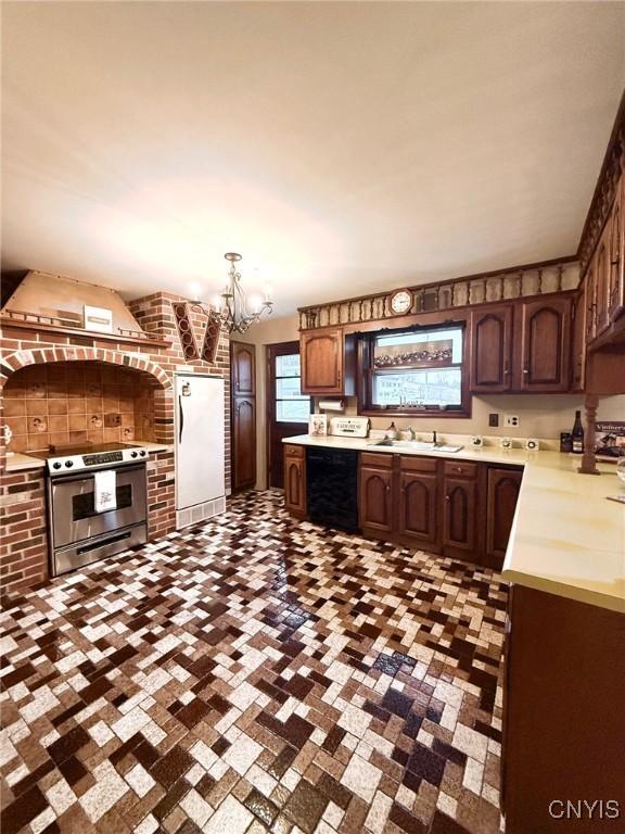 kitchen featuring stainless steel electric range, dishwasher, an inviting chandelier, wall chimney range hood, and white fridge