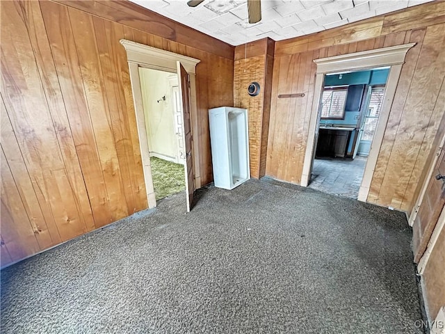 hallway featuring wood walls and dark colored carpet