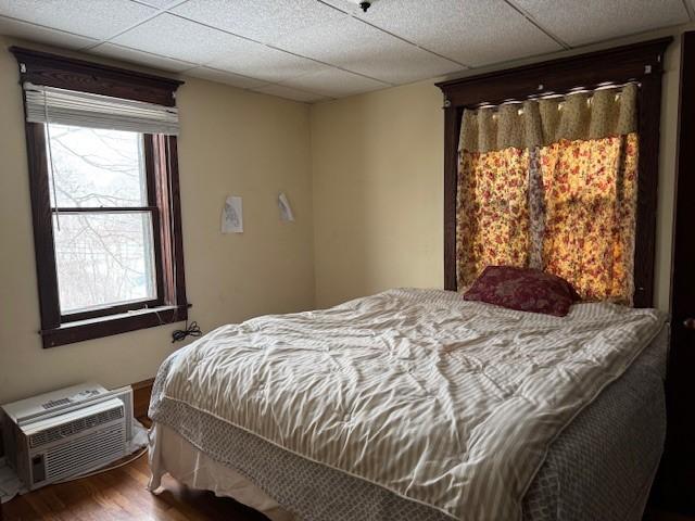 bedroom featuring a wall mounted AC, wood finished floors, and a paneled ceiling