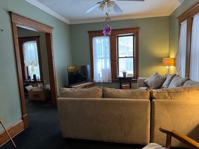 living room featuring crown molding, baseboards, dark carpet, and ceiling fan