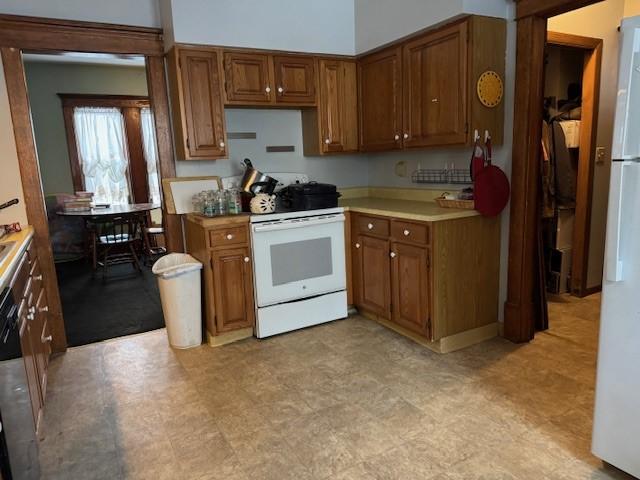 kitchen with brown cabinetry, light floors, white appliances, and light countertops