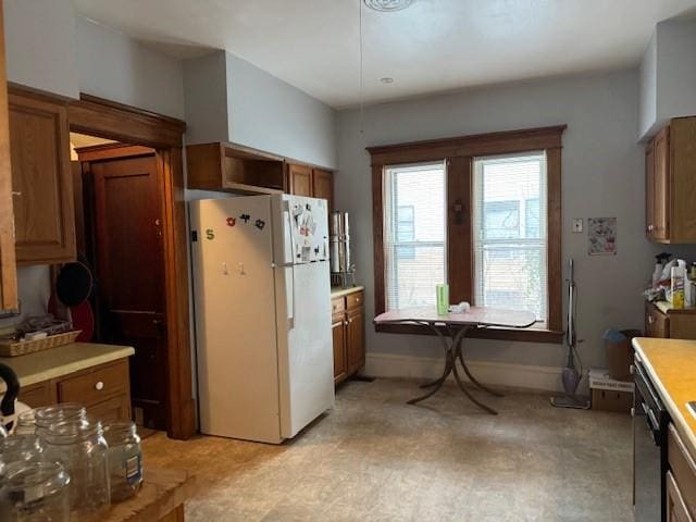 kitchen featuring brown cabinetry, light countertops, freestanding refrigerator, and baseboards