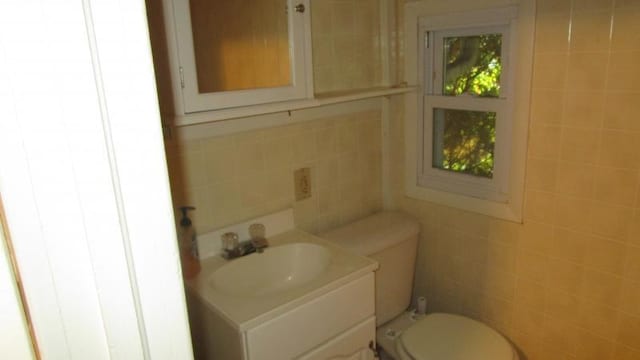 half bathroom with toilet, tile walls, and vanity