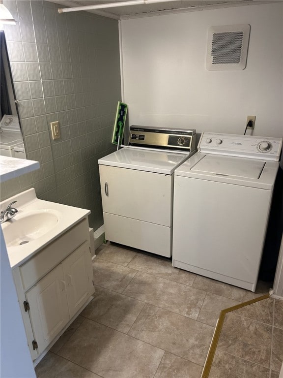 clothes washing area featuring washer and dryer, tile walls, laundry area, and a sink