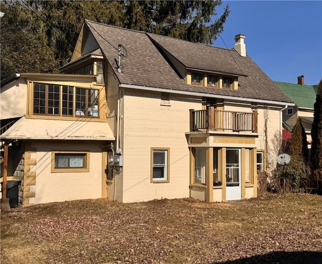 rear view of house with a chimney, a balcony, and roof with shingles