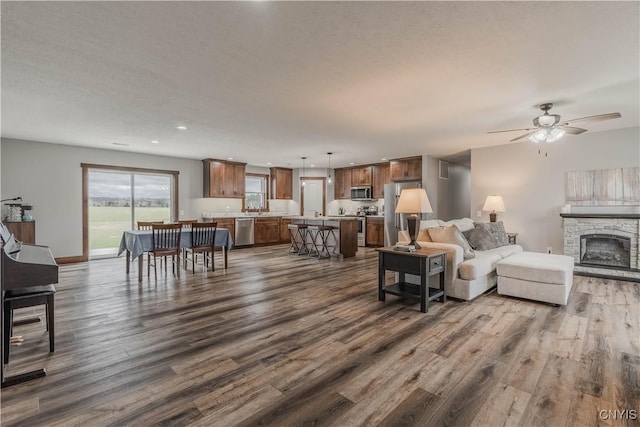 living room with a stone fireplace, ceiling fan, dark hardwood / wood-style flooring, and a textured ceiling