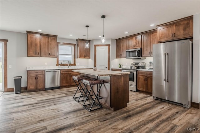 kitchen with a kitchen bar, stainless steel appliances, wood-type flooring, decorative light fixtures, and a center island