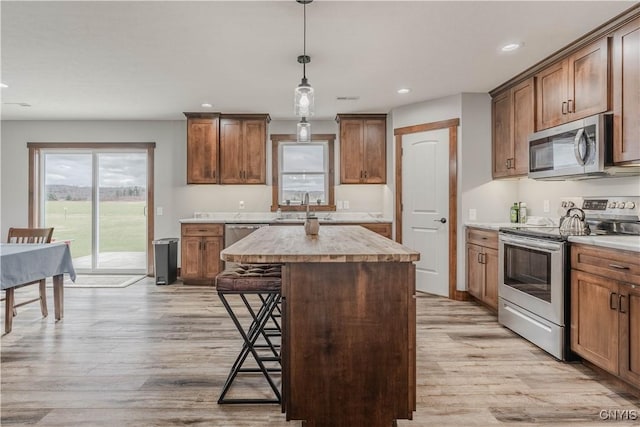 kitchen with a center island, stainless steel appliances, light hardwood / wood-style floors, decorative light fixtures, and a breakfast bar area