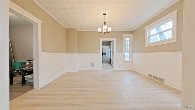 unfurnished room featuring light wood-type flooring, crown molding, and a notable chandelier