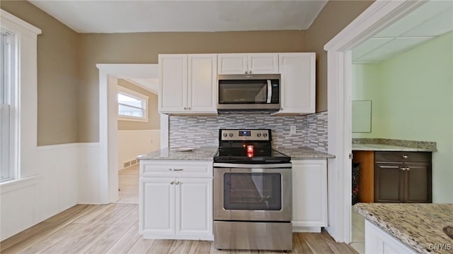 kitchen featuring light stone countertops, white cabinetry, stainless steel appliances, light hardwood / wood-style flooring, and backsplash