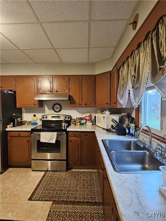 kitchen featuring a paneled ceiling, stainless steel range with electric cooktop, black refrigerator, sink, and light tile patterned floors