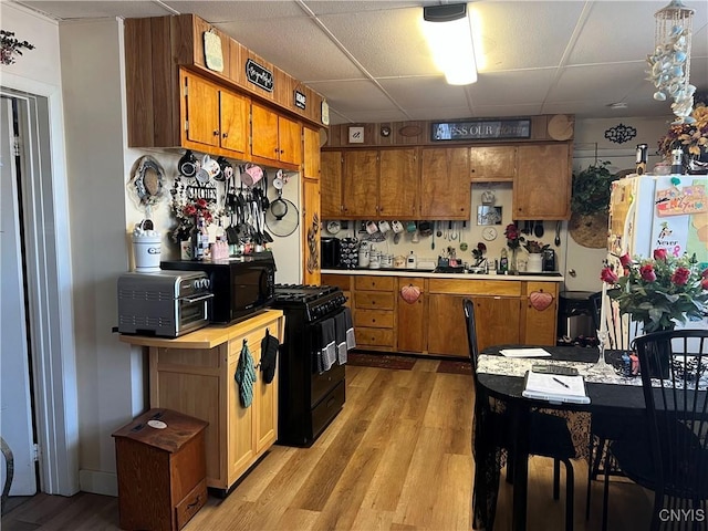 kitchen with light wood-type flooring, a drop ceiling, and black appliances