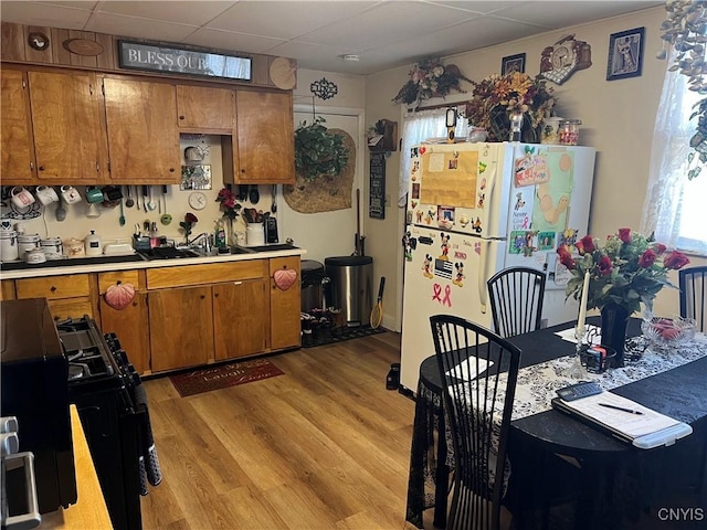 kitchen with a drop ceiling, brown cabinets, light wood-type flooring, and freestanding refrigerator