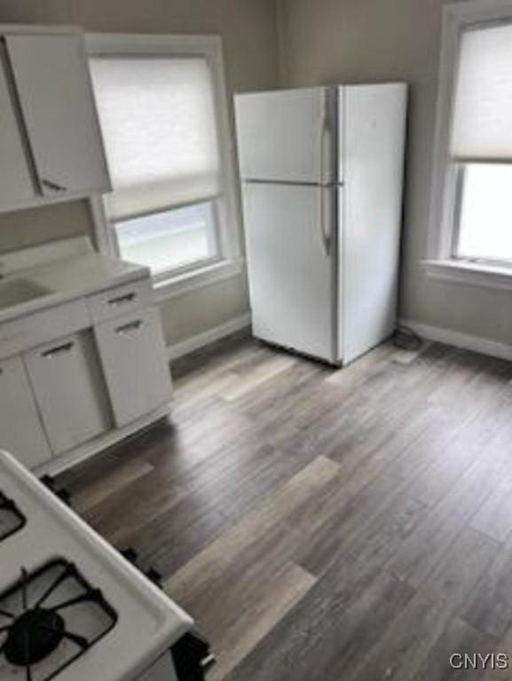 kitchen featuring light wood finished floors, white appliances, white cabinetry, and baseboards