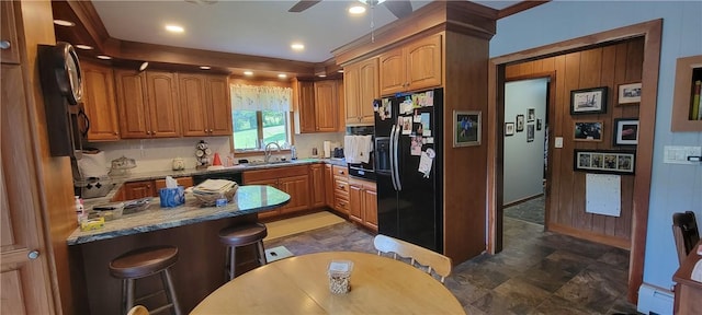 kitchen with black appliances, a kitchen breakfast bar, sink, ceiling fan, and light stone counters