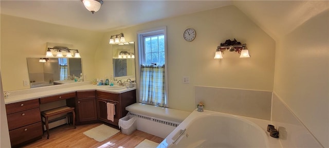 bathroom featuring a baseboard heating unit, hardwood / wood-style floors, lofted ceiling, a bathtub, and vanity