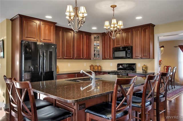 kitchen featuring a kitchen island with sink, black appliances, sink, dark hardwood / wood-style flooring, and a chandelier