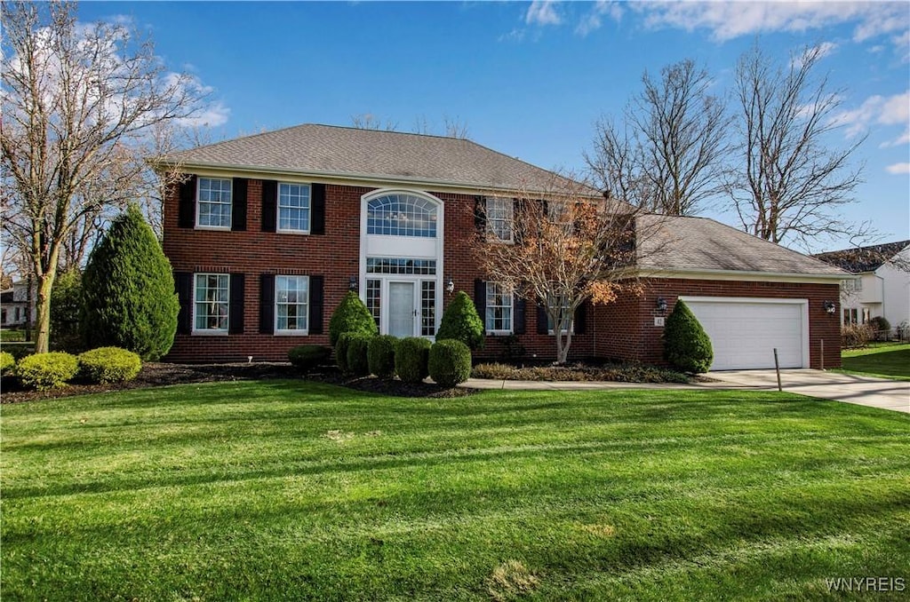 colonial-style house featuring a front yard, concrete driveway, brick siding, and an attached garage