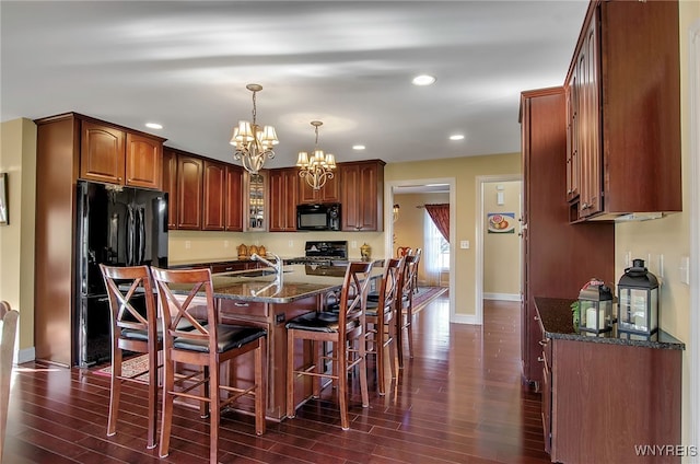 kitchen with a breakfast bar, black appliances, dark hardwood / wood-style floors, and an inviting chandelier