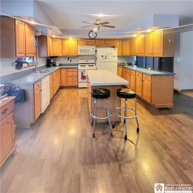 kitchen with a center island, sink, light hardwood / wood-style floors, white appliances, and a breakfast bar area