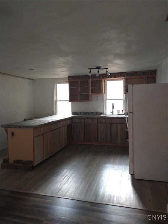 kitchen with kitchen peninsula, gas cooktop, dark wood-type flooring, sink, and white fridge