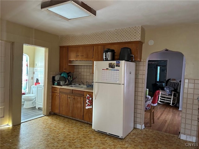 kitchen featuring light wood-type flooring, white fridge, tile walls, and sink