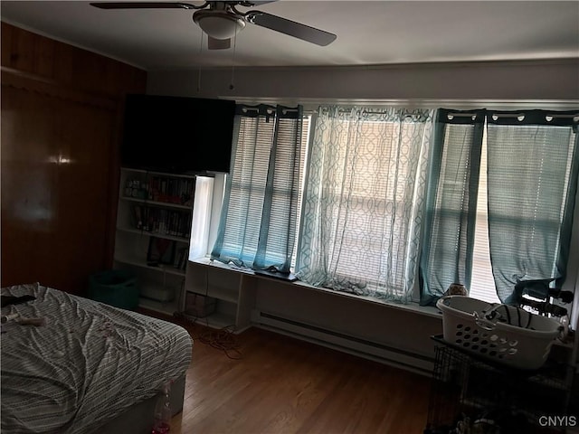 bedroom featuring ceiling fan, hardwood / wood-style floors, a baseboard heating unit, and wooden walls