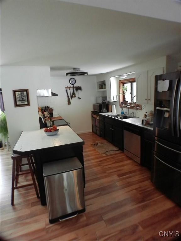 kitchen with dishwasher, black refrigerator with ice dispenser, a kitchen breakfast bar, sink, and dark hardwood / wood-style floors