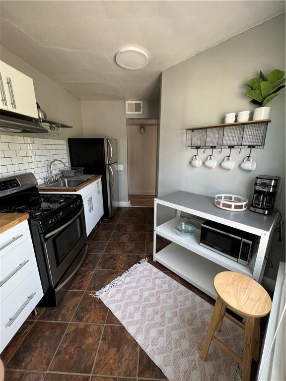 kitchen with wooden counters, appliances with stainless steel finishes, tasteful backsplash, sink, and white cabinets