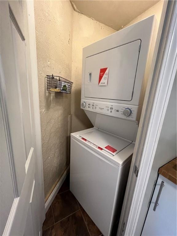 washroom with dark tile patterned floors and stacked washer and dryer