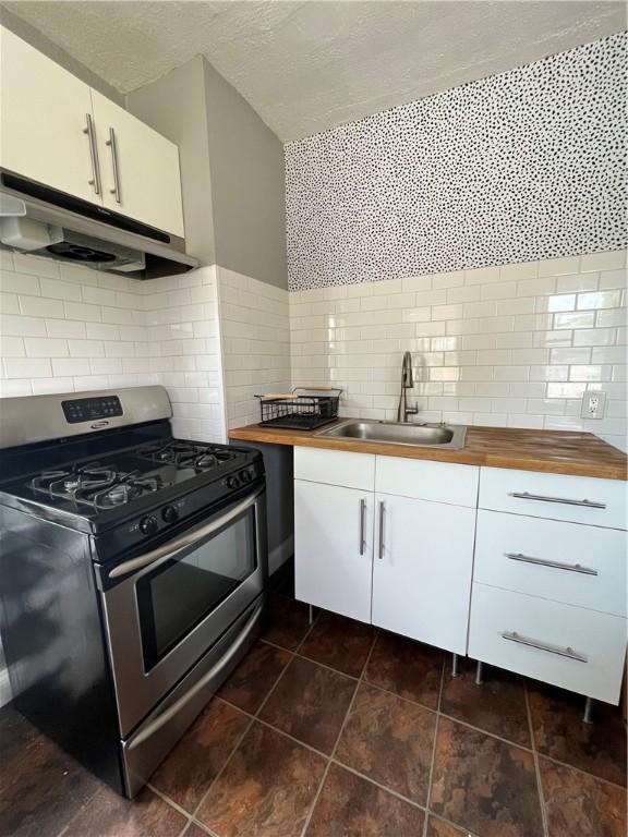 kitchen with butcher block countertops, stainless steel gas range oven, sink, and white cabinets