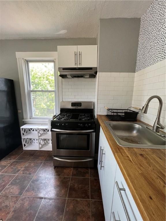 kitchen with wooden counters, white cabinets, black refrigerator, sink, and stainless steel gas range