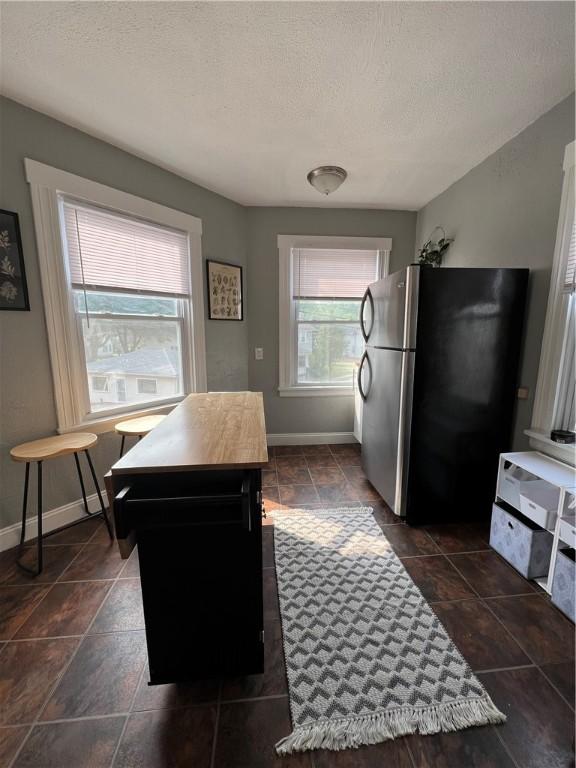 interior space featuring a textured ceiling, a center island, stainless steel refrigerator, and butcher block counters