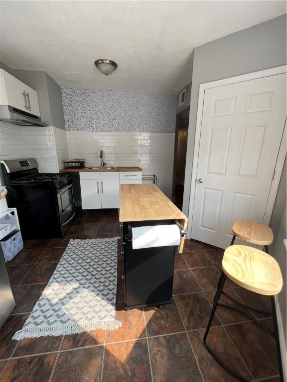 kitchen featuring stainless steel gas range oven, sink, white cabinets, and tile walls